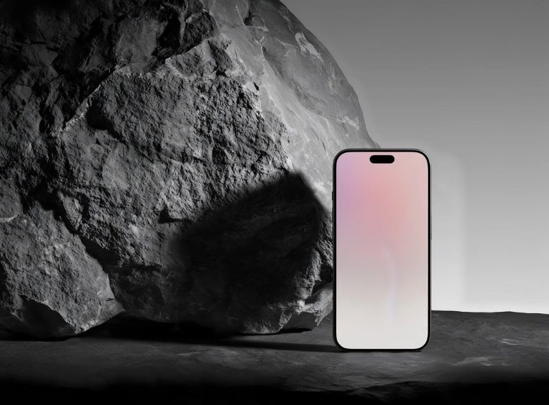 Start on the reference image: a dark phone standing upright against a large rough black rock on a stone ledge, in moody…
